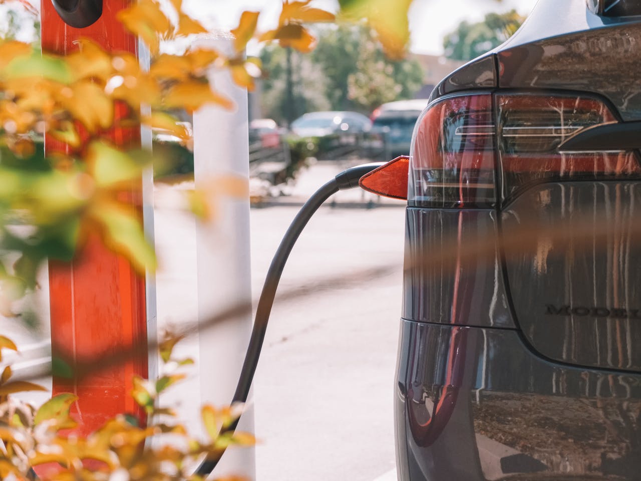 heros-img Close-up of an electric car charging at a station with blurred cars in the background.